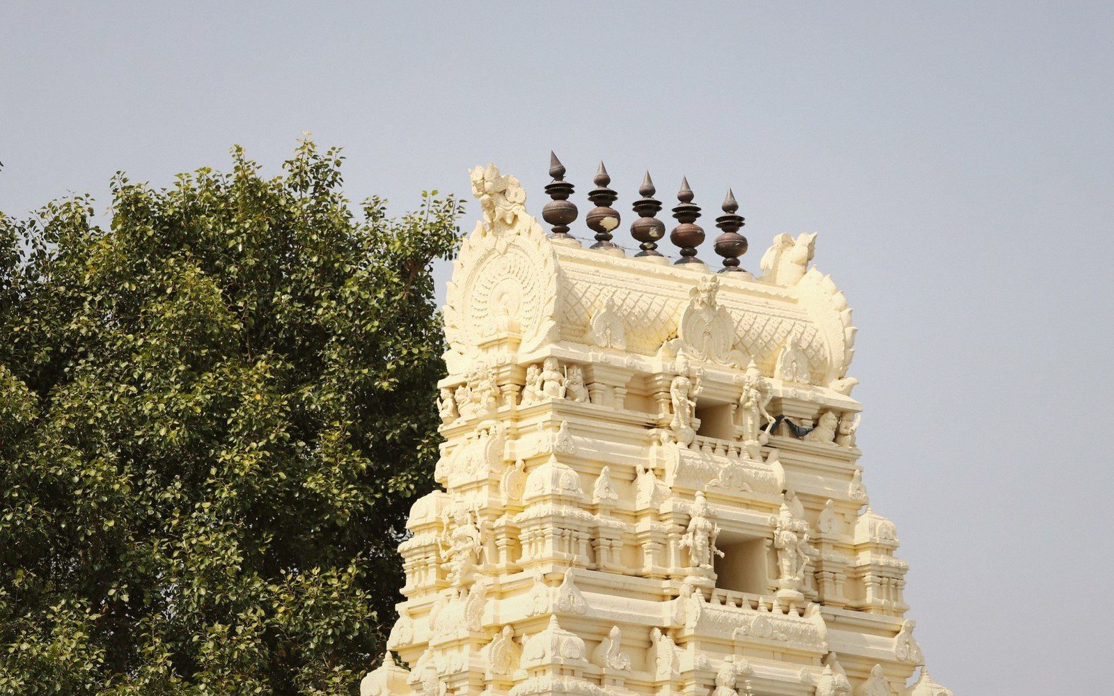 Rows of dark pot-shaped finials top a tiered gopuram tower carved with deity figures
