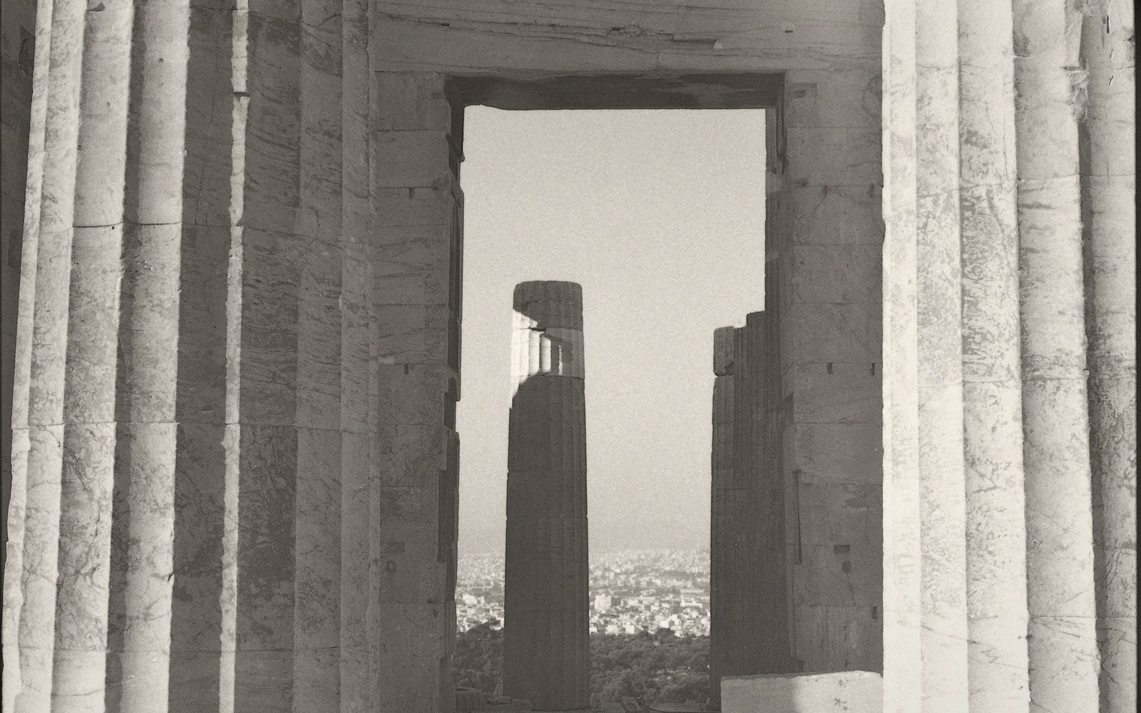 Ancient stone columns framed through a doorway overlook a distant cityscape below