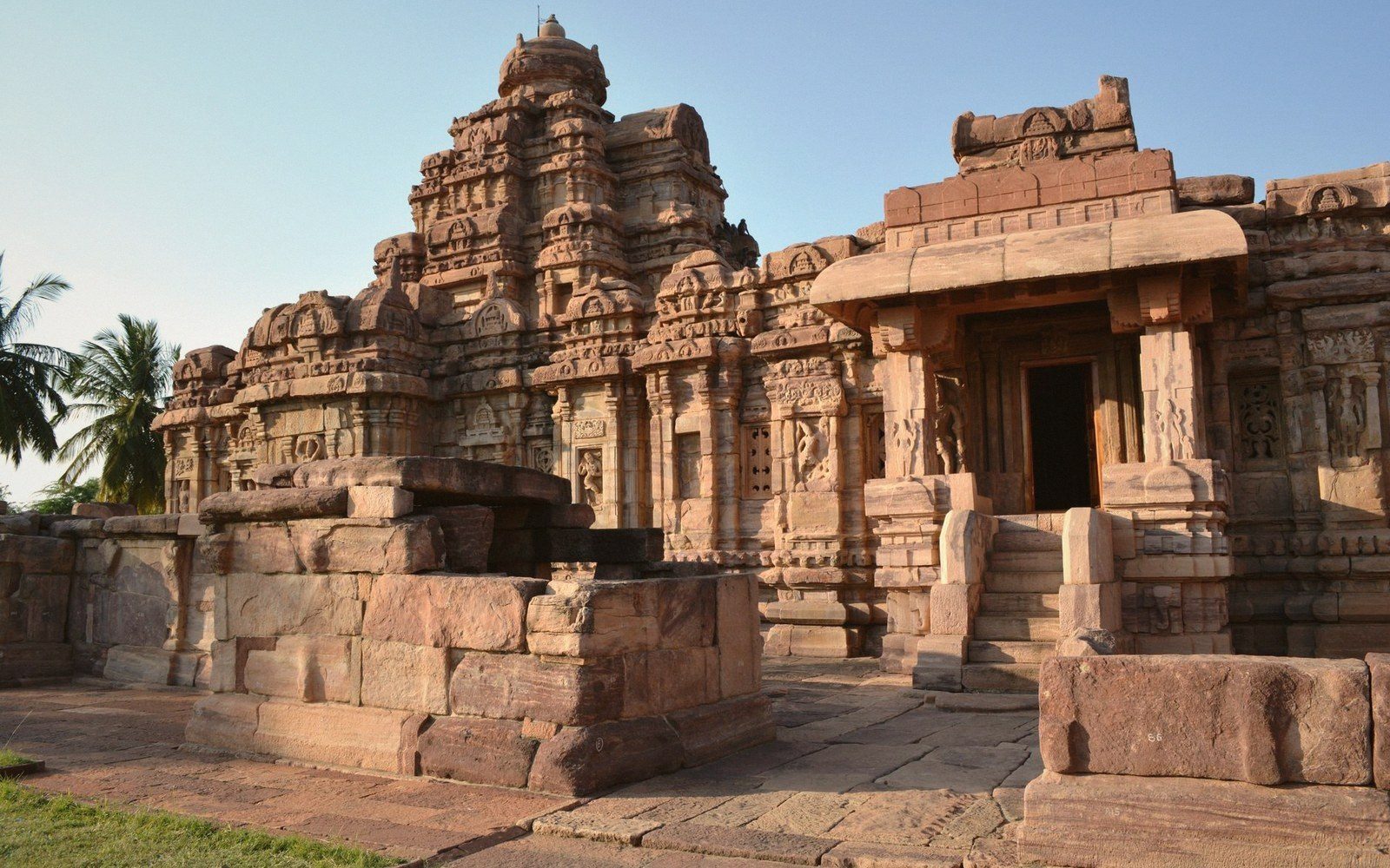 Carved stone temple with a tiered tower and pillared entrance porch under a clear sky