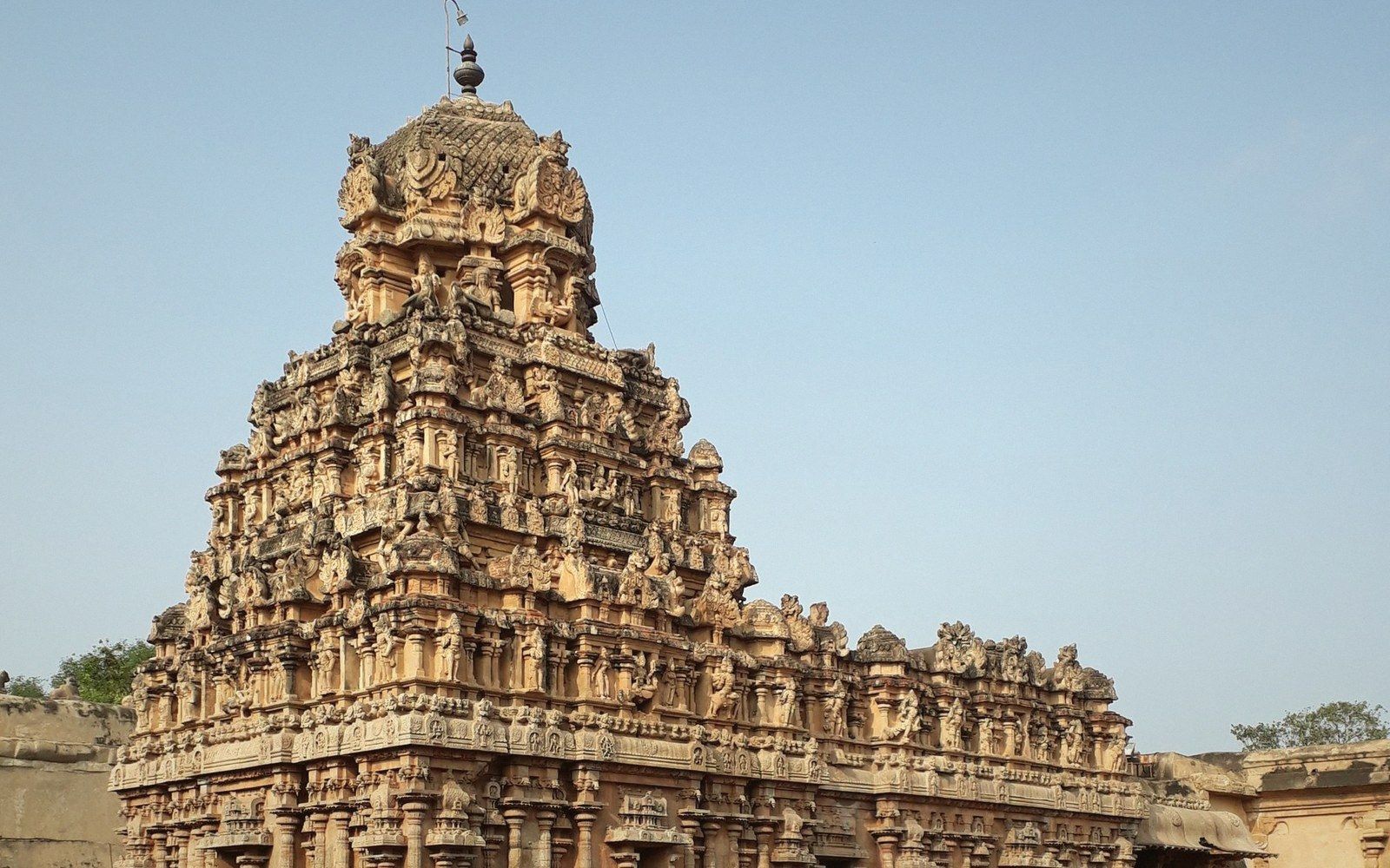 Tiered stone gopuram tower with tiers of carved figures rising against a clear sky