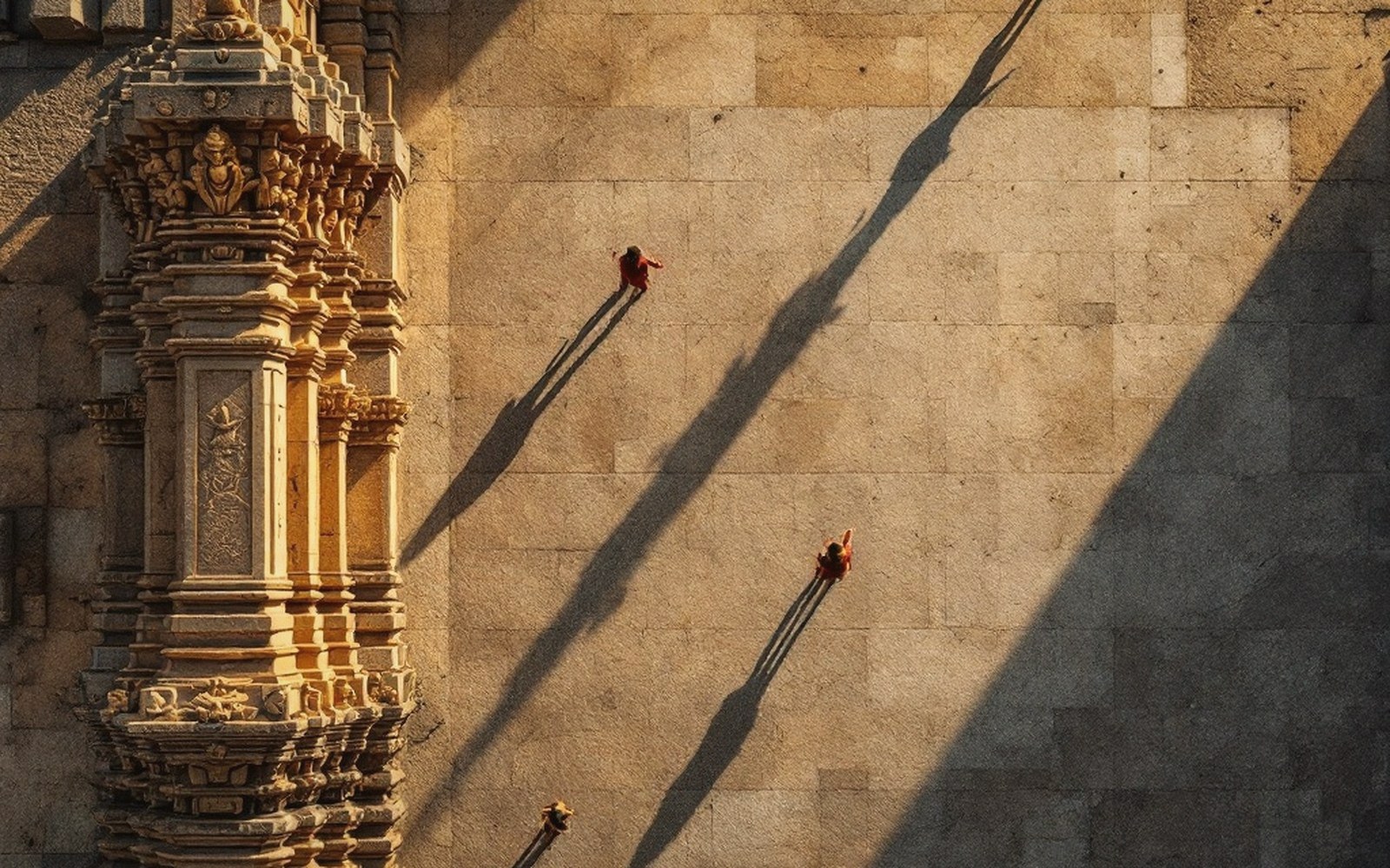 Aerial view of temple visitors casting long shadows beside an ornately carved stone tower