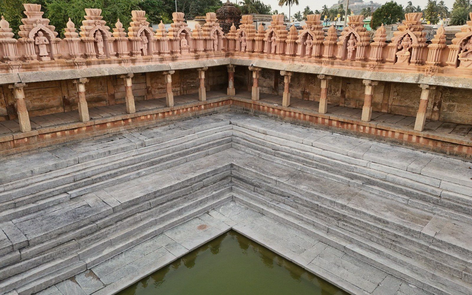 Stepped stone temple tank with carved pillared corridor and small pool at center