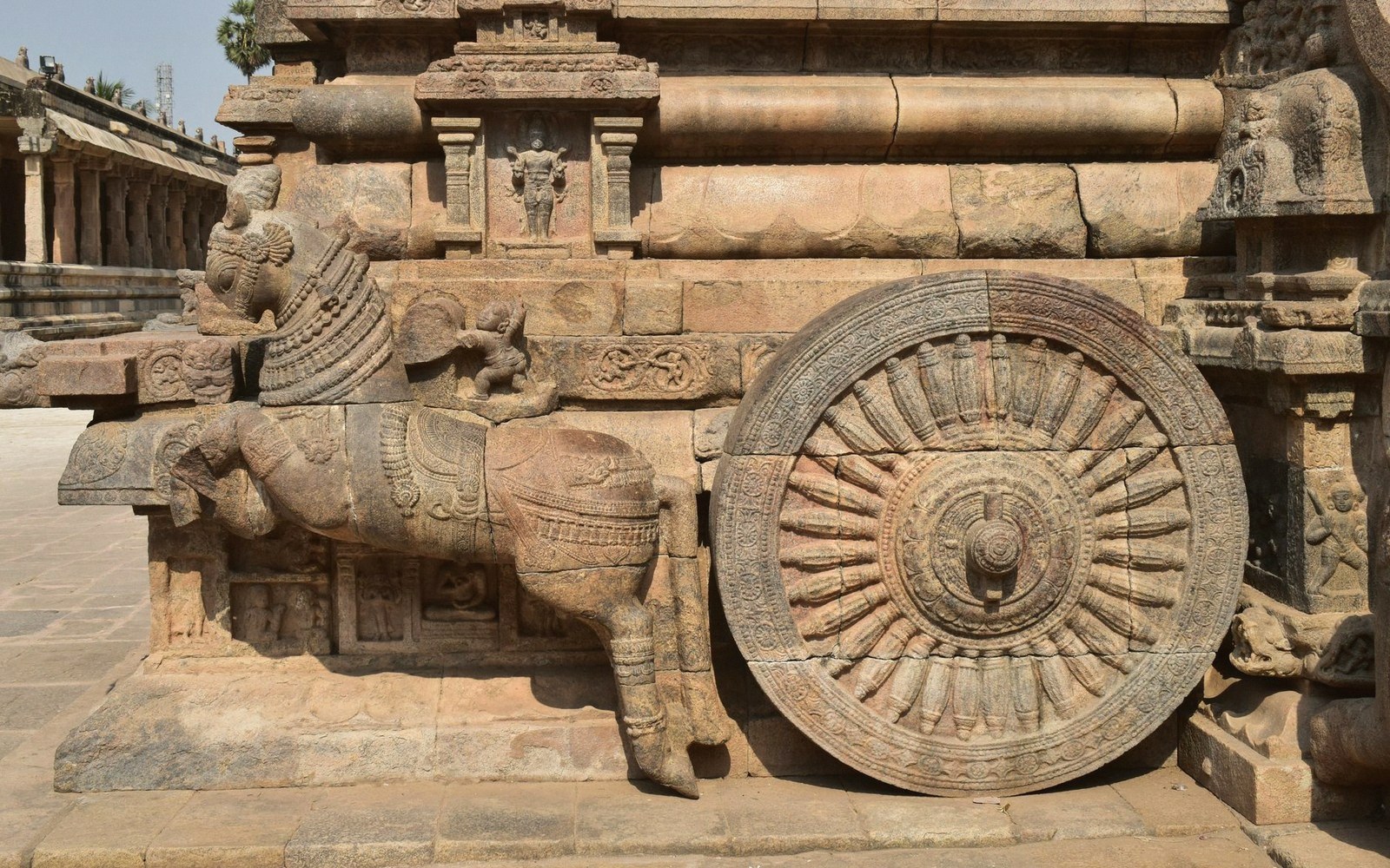 Stone-carved chariot wheel and horse sculpture on a temple's base structure
